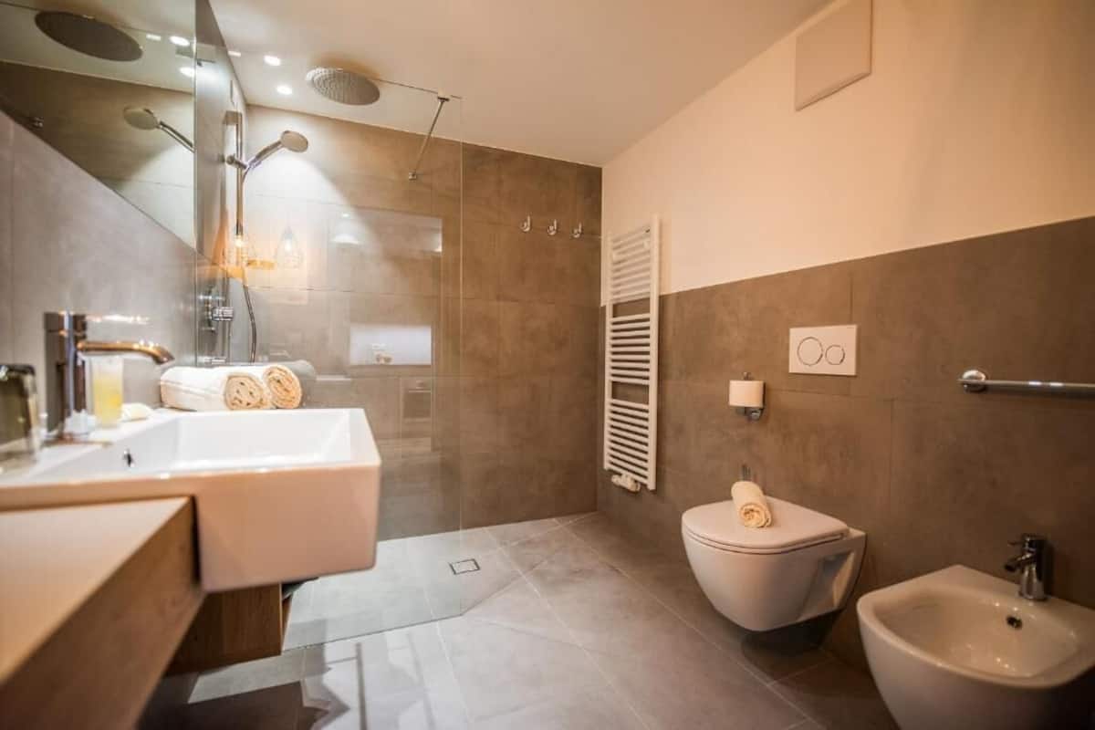A modern bathroom with a glass-enclosed shower, a white sink, a toilet, and a bidet.