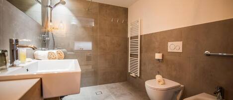 A modern bathroom with a glass-enclosed shower, a white sink, a toilet, and a bidet.