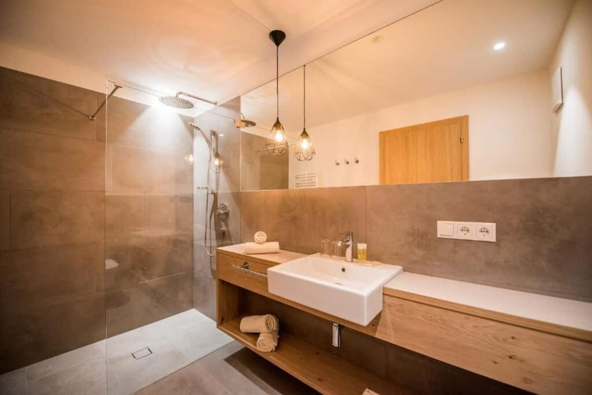 A modern bathroom with a glass shower enclosure, a wooden vanity, and pendant lighting.