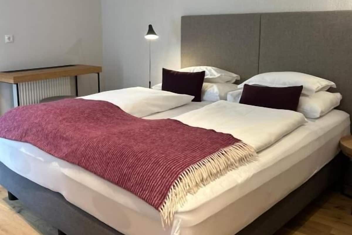 A single bed with a headboard, a bedside table, a floor lamp, and a red throw blanket.