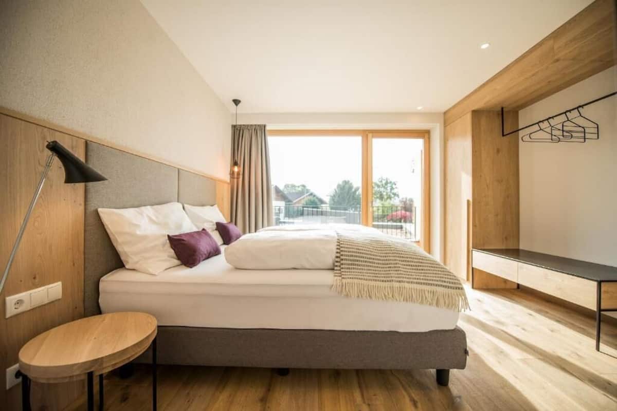 A modern bedroom with a bed, bedside table, and a view of the outdoors.
