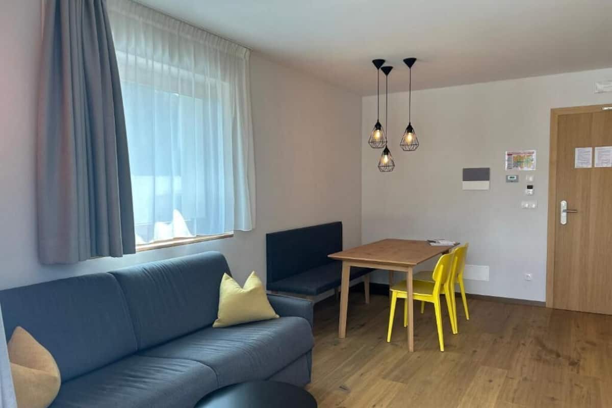 A modern living room with a sofa, a dining table, yellow chairs, a small round table, and pendant lights.