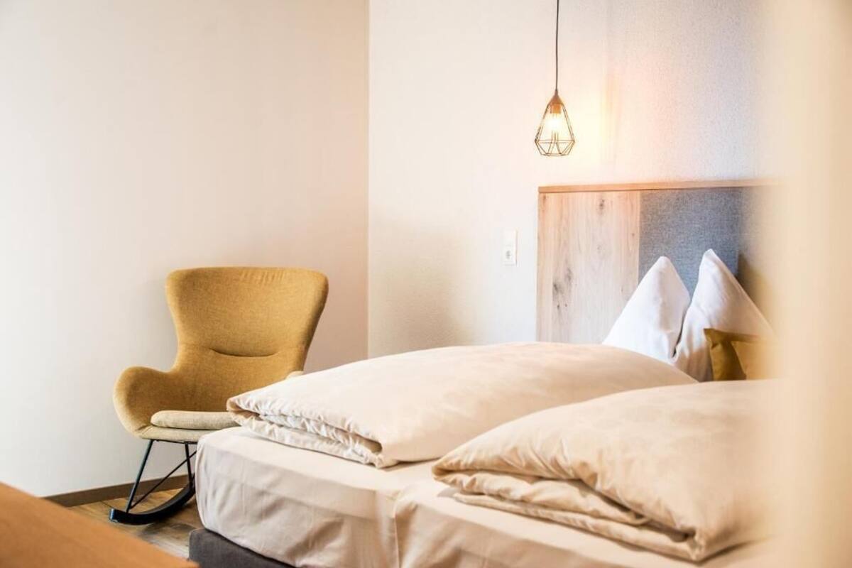 A bedroom with a bed, a rocking chair, and a hanging light fixture.
