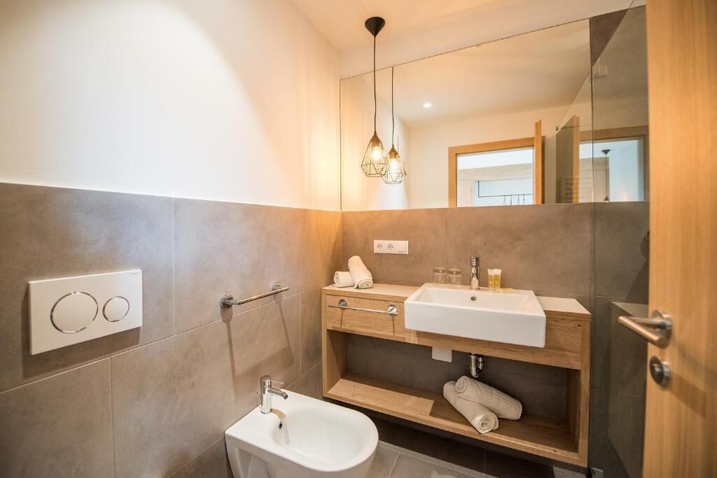 Une salle de bain moderne équipée d’un bidet, d’un lavabo, d’un miroir et d’un porte-serviettes.