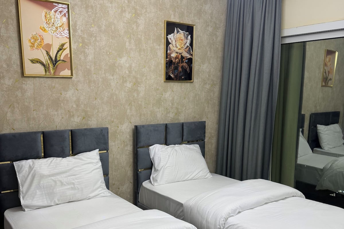 Une chambre d’hôtel avec deux lits, un grand miroir et deux tableaux représentant des motifs floraux, encadrés et accrochés au mur.