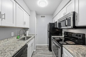 A kitchen with white cabinets, a stainless steel refrigerator, a microwave, and a black stove. - Great 1BR Mid-Term Apartment (Denton)