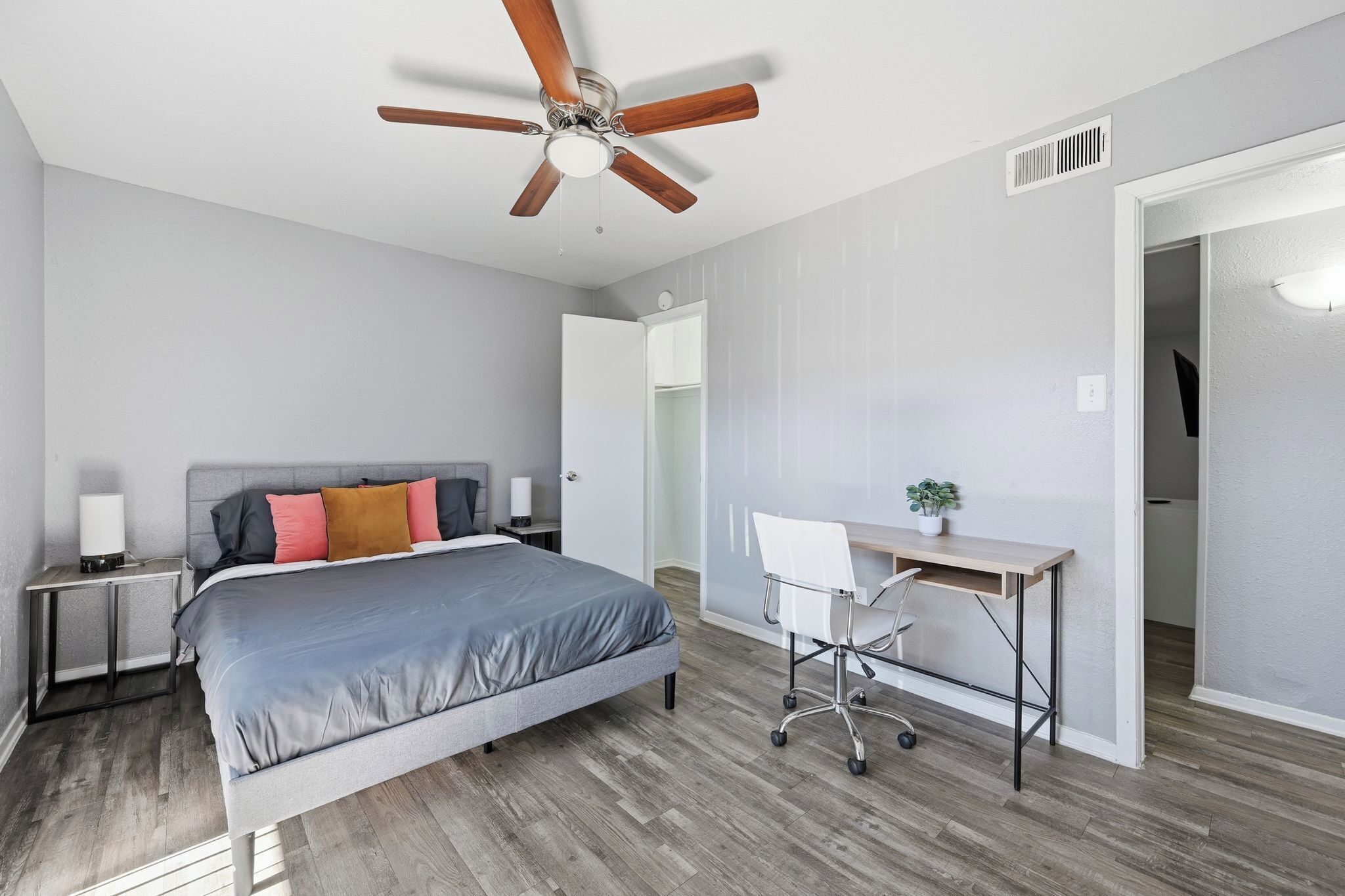 A bedroom with a bed, a desk, a chair, a ceiling fan, and a nightstand.