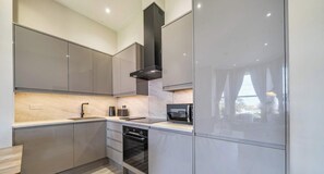 A modern kitchen with grey cabinets, a built-in oven, and a microwave. - Coastal Comfort, 2 Bed with Sea Views (Portsmouth)