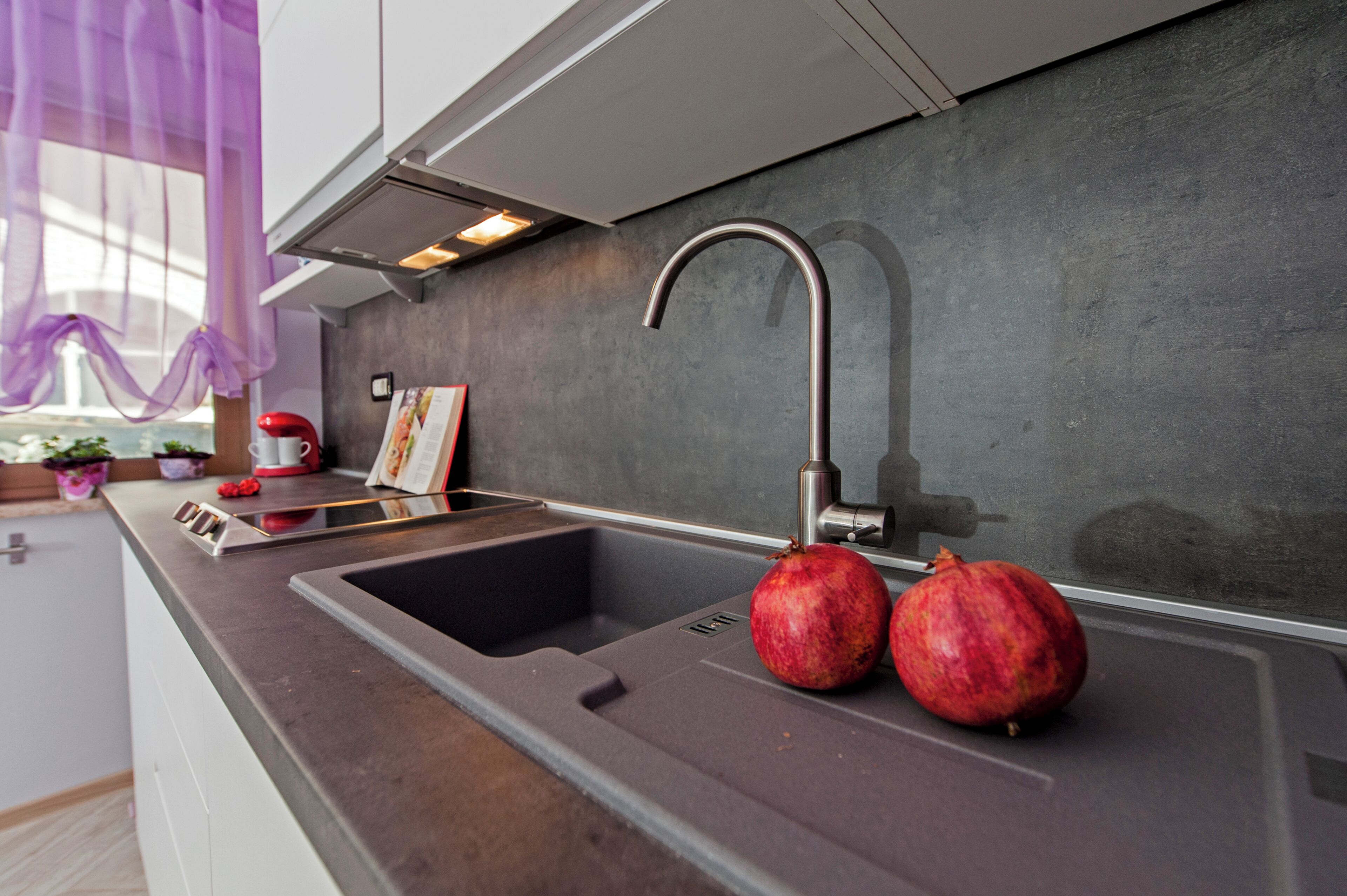 Una cocina moderna con un lavamanos de acero inoxidable, una granada y un hervidor rojo.