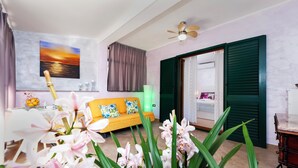 Ein Wohnzimmer mit Sofa, einem Gemälde, einem Deckenventilator und Blick durch eine Tür.