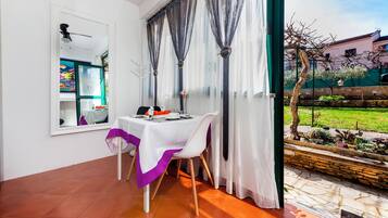Uma área de refeições com uma mesa posta para dois, uma janela com cortinas e vista para um jardim.