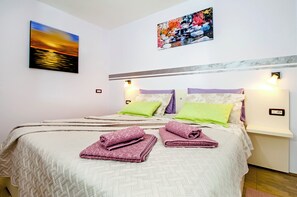 Una cama bien hecha con almohadas, un cuadro de un atardecer y una lámpara de pared.