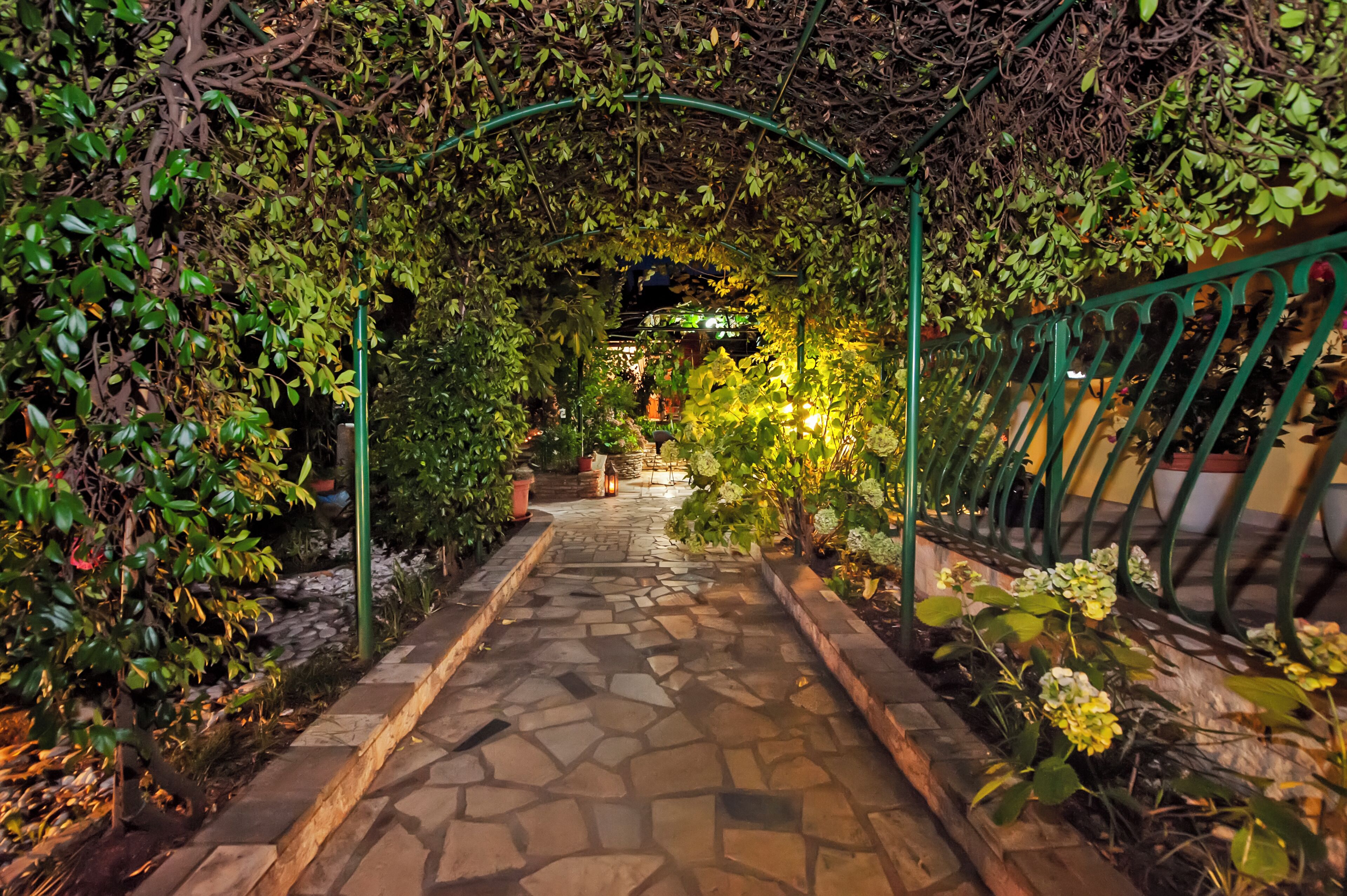 Un sendero de piedra que atraviesa un jardín exuberante con un arco de metal verde.