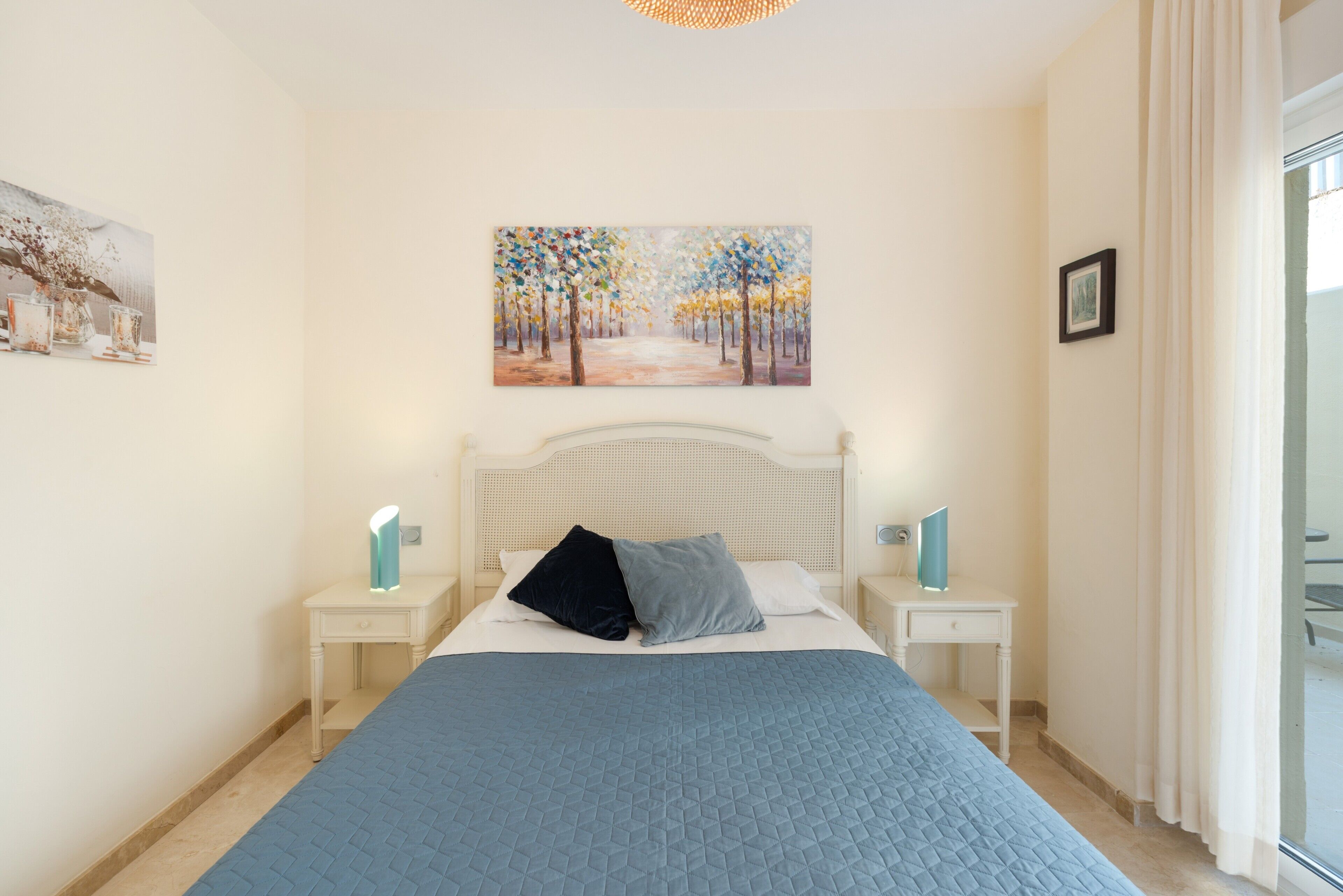 Une chambre à coucher avec un lit, deux tables de chevet, une commode, un tableau au mur et une fenêtre avec des rideaux.