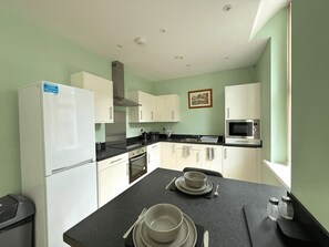 A compact kitchen with white cabinets, a black countertop, a microwave, and a stove. - Beautiful 2-bed flat In Vibrant City Centre (Sheffield)