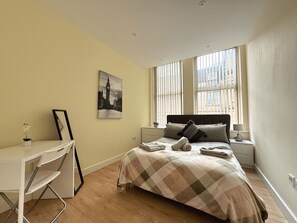 A bedroom with a bed, bedside tables, a desk, and a window with blinds. - Beautiful 2-bed flat In Vibrant City Centre (Sheffield)
