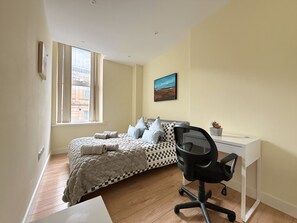 A bedroom with a bed, a desk, a chair, a window, and a painting on the wall. - Beautiful 2-bed flat In Vibrant City Centre (Sheffield)