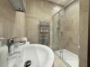 A modern bathroom with a glass-enclosed shower, a white sink, and a towel rack. - Beautiful 2-bed flat In Vibrant City Centre (Sheffield)