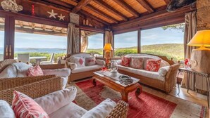 Amplia sala de estar con mobiliario de mimbre, techo de madera y vistas del paisaje.
