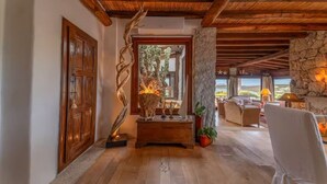 Techo de madera, un pilar de piedra, una puerta de madera, una chimenea y una vista por un vano.