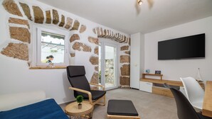 Quarto com paredes de pedra, televisão de tela plana, sofá, mesa pequena com uma planta e um banco de madeira.