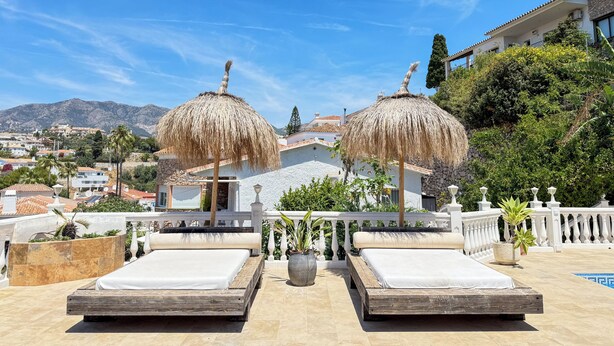 Una terraza en la azotea con dos camas, una piscina y vistas a un pueblo y montañas.