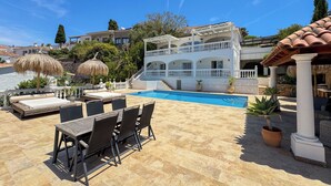 Un área de piscina con sillones de descanso, una mesa de comedor y una pérgola.