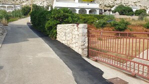 Un quartier résidentiel avec une route asphaltée, un mur en pierre et un portail en métal rouge.