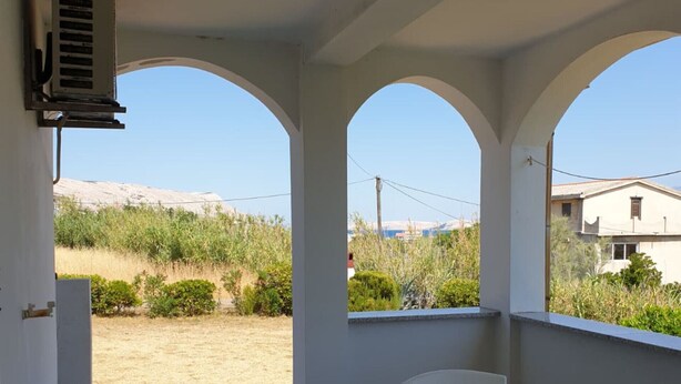 Une terrasse couverte avec une table et des chaises, une vue sur un paysage aride et un bâtiment en arrière-plan.