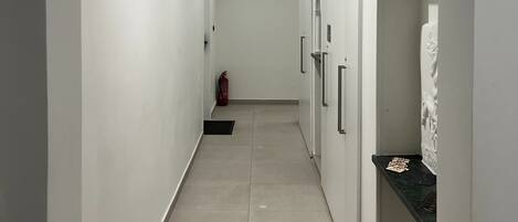 A hallway with an arched ceiling, recessed lighting, a fire extinguisher, and a tiled floor.