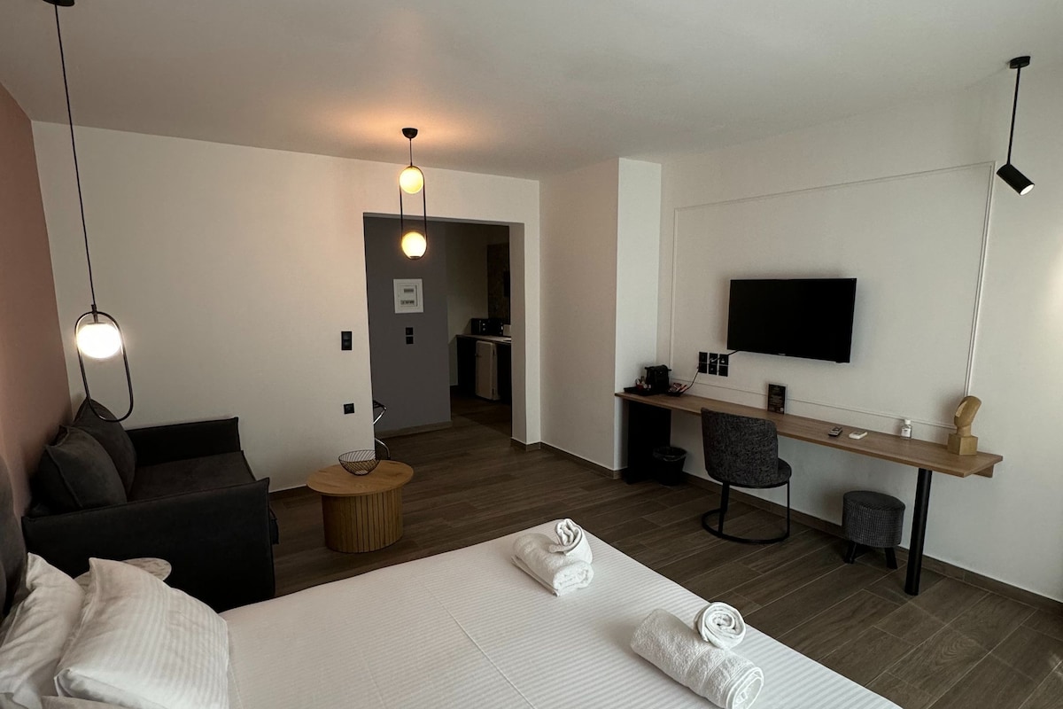 A hotel room with a large bed, a desk, a TV, and a seating area with a sofa and chairs.