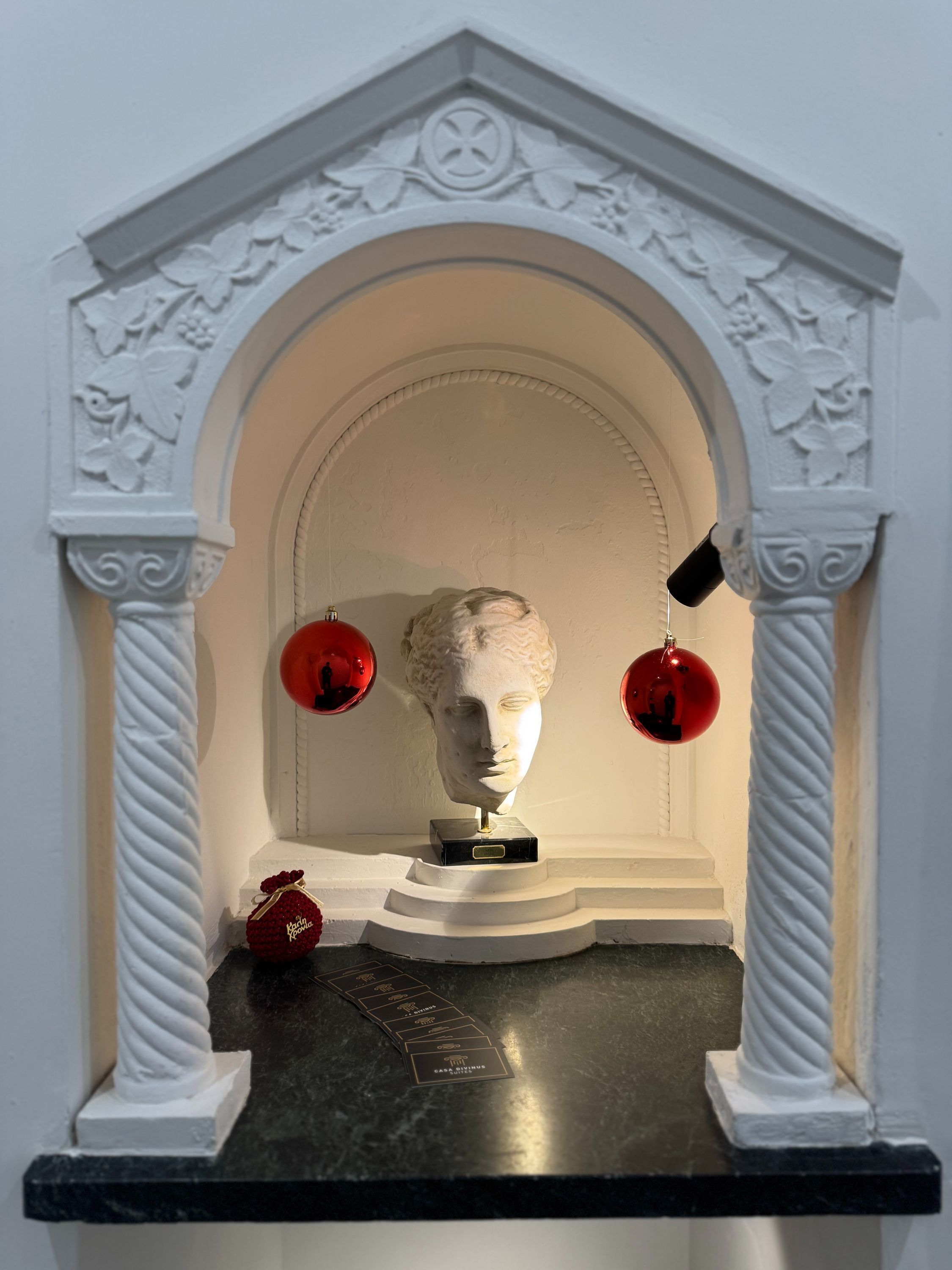 A marble bust on a pedestal, a red ornament, and a small red gift box.