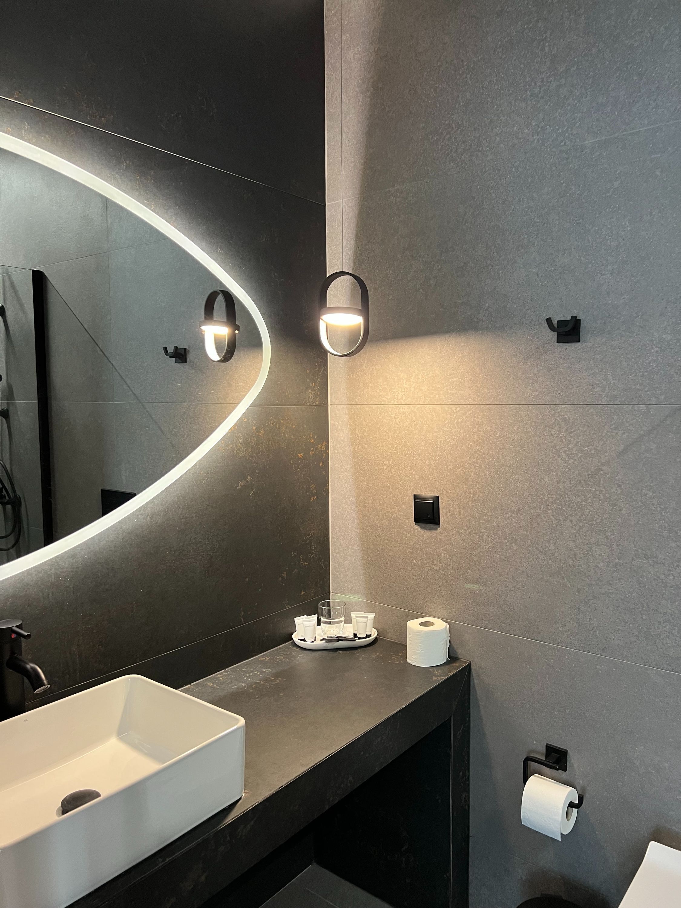 A modern bathroom with a large mirror, a white sink, and a towel rack.