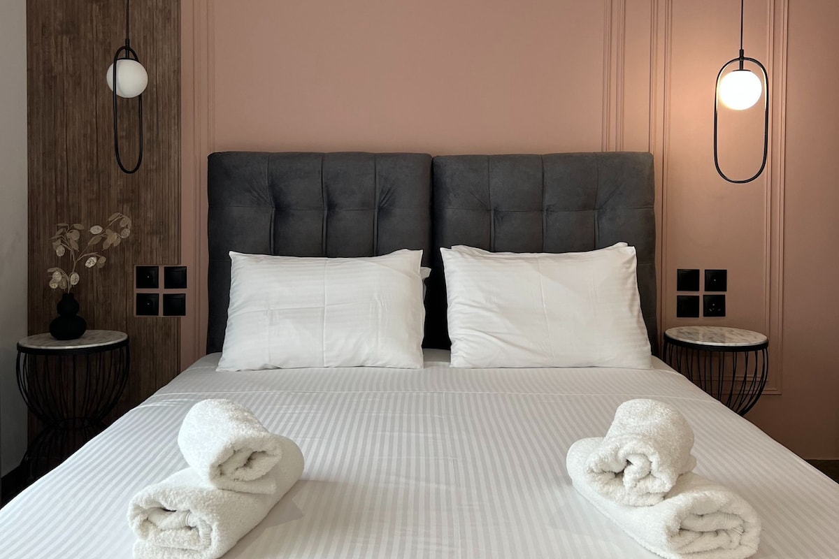 A hotel room with a large bed, two bedside tables, a wall-mounted light fixture, and a small round table with a vase.