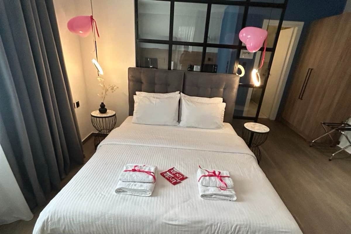 A neatly made bed with white linens, two pillows, and two towels with pink ribbons.