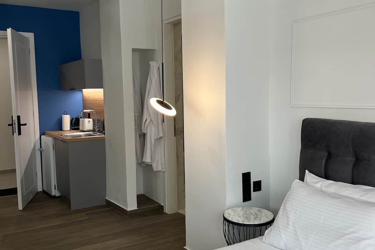 A hotel room with a bed, a bedside table, a hanging light fixture, a bathroom visible through an open door, and a small round table with a chair.