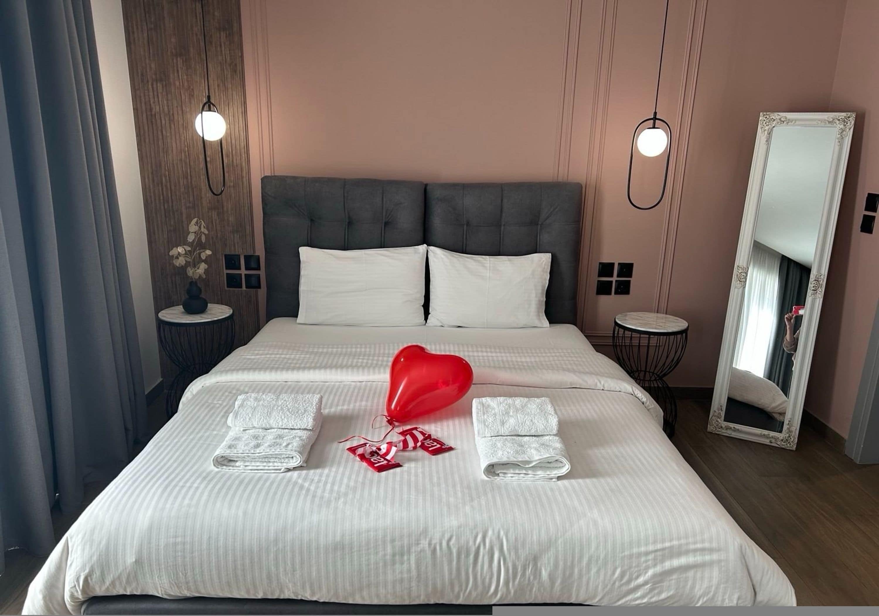 A hotel room with a large bed, two bedside tables, a mirror, and a wall-mounted light fixture.