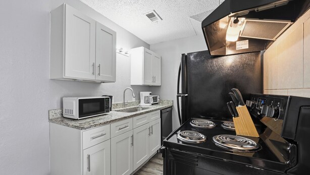 A kitchen with white cabinets, a black stove, a microwave, and a coffee maker. - Cozy 1BR townhome perfect for relaxing stays (Arlington)