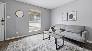 A living room with a grey sofa, a coffee table, a round mirror, and abstract wall art. - Cozy 1BR townhome perfect for relaxing stays (Arlington)