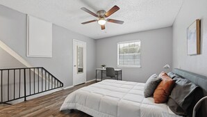 A bedroom with a bed, a desk, a chair, a ceiling fan, a window with blinds, and a staircase. - Cozy 1BR townhome perfect for relaxing stays (Arlington)