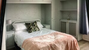 Ein Schlafzimmer mit einem Bett, einem Nachttisch, einer Lampe, einem Heizkörper und einer Tür.