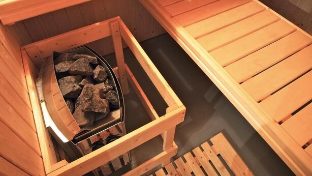 A sauna with wooden benches and a metal container holding rocks. - LE RELAIS DE LA FORGE (Selonnet)