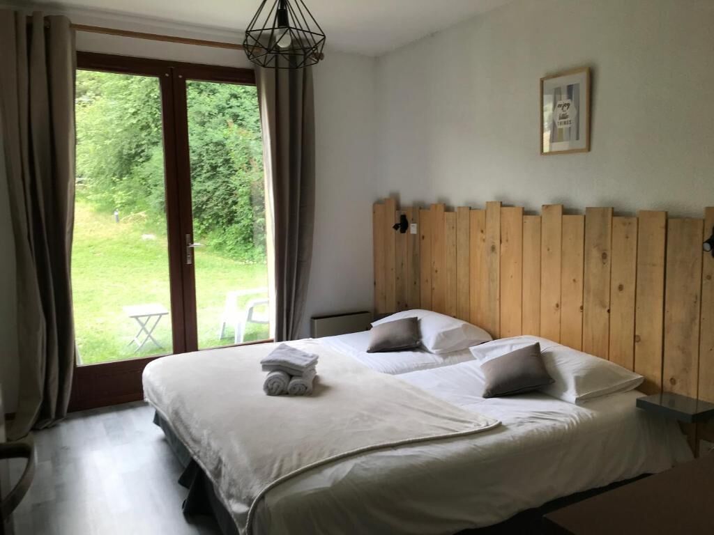 A bedroom with a large bed, wooden headboard, a view of greenery, and a framed picture on the wall.