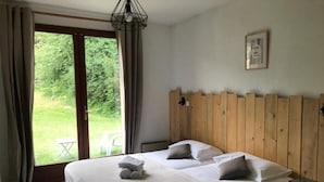 A bedroom with a large bed, wooden headboard, a view of greenery, and a framed picture on the wall. - LE RELAIS DE LA FORGE (Selonnet)