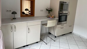 Una cucina compatta con forno a incasso, un angolo ristoro con una sedia e uno specchio sopra il bancone.
