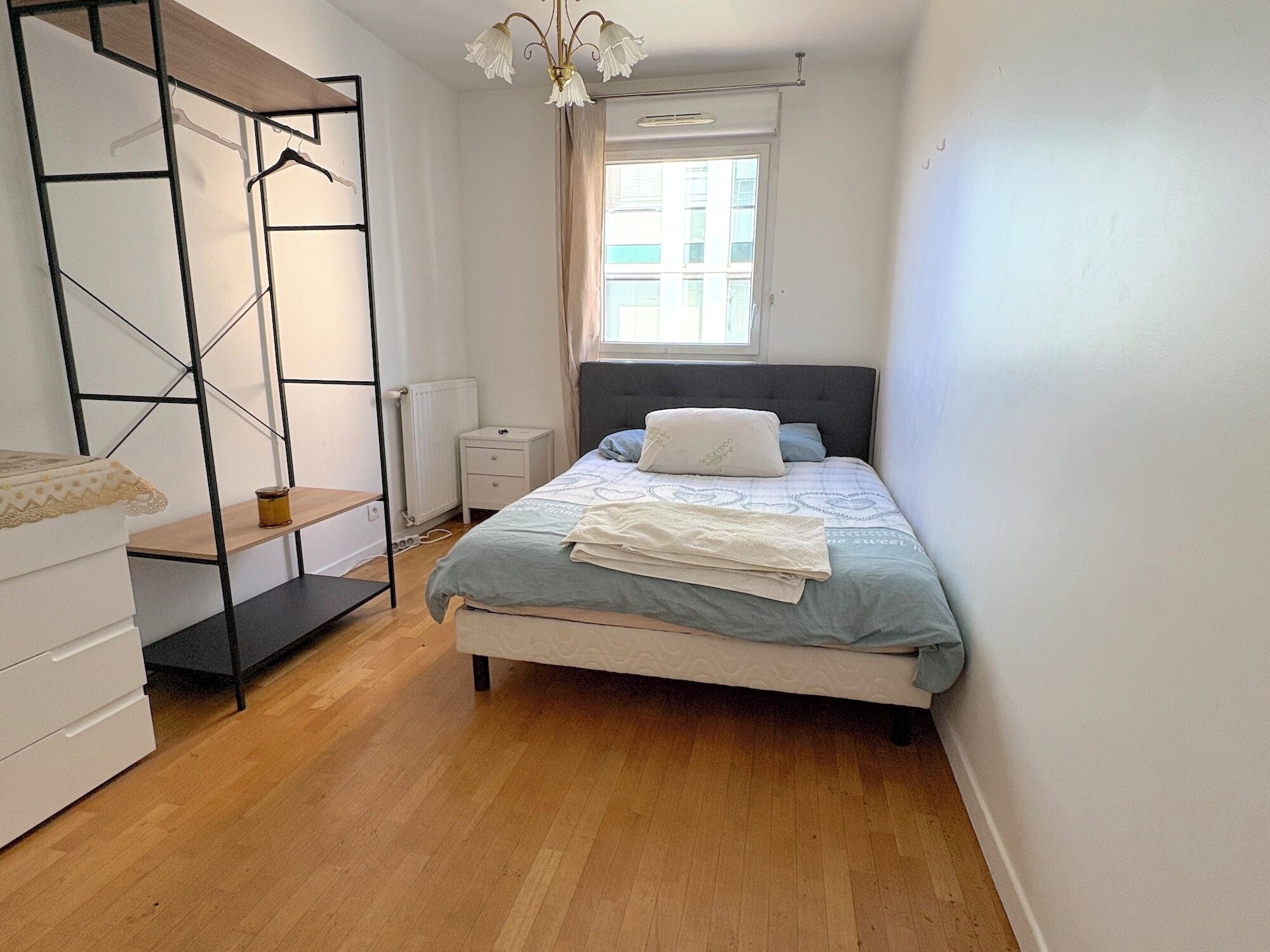 A bedroom with a bed, a wardrobe, a nightstand, and a window.
