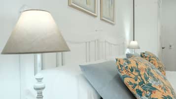 Un lit avec une literie blanche, un oreiller gris et un oreiller à motifs floraux. Une lampe se trouve sur une table de chevet.