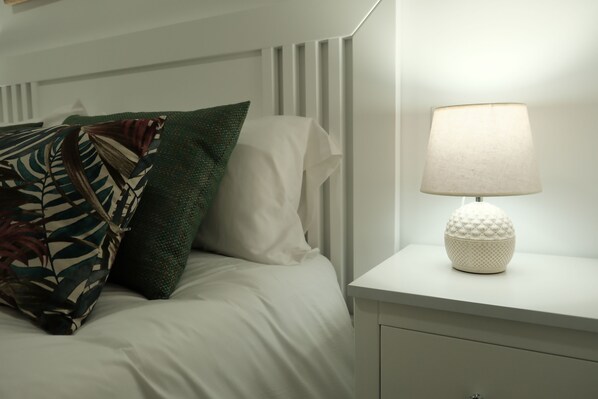 A neatly made bed with a white comforter, a green leaf-patterned pillow, and a white pillow. There is a white bedside table with a white lamp. - Balcones a San Pedro (Osuna)