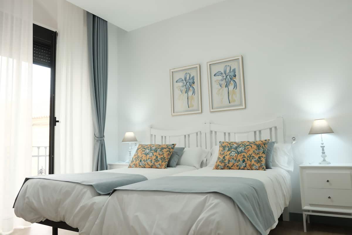 A double bed with a white headboard, two bedside tables with lamps, and a window with curtains.