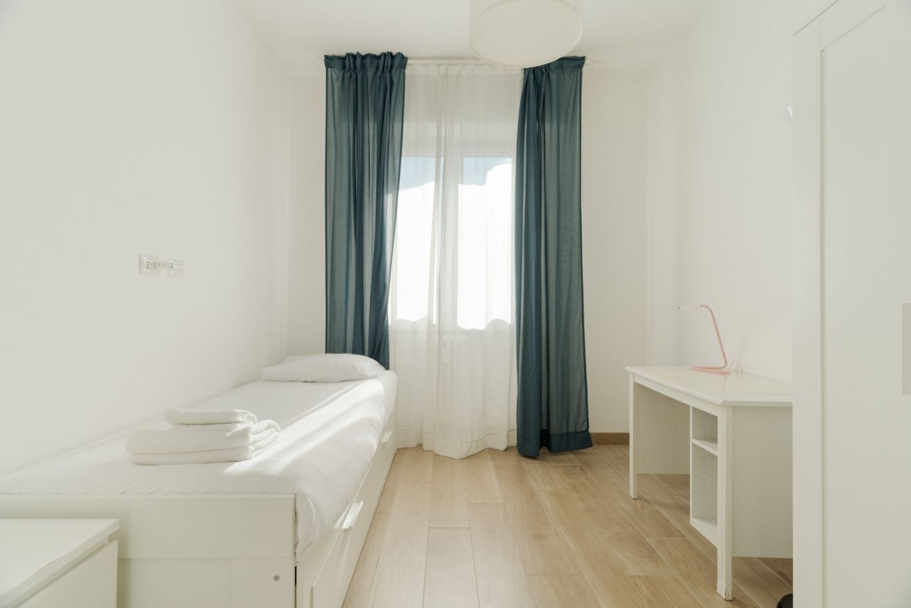 Een slaapkamer met een bed, een bureau en een raam met gordijnen.